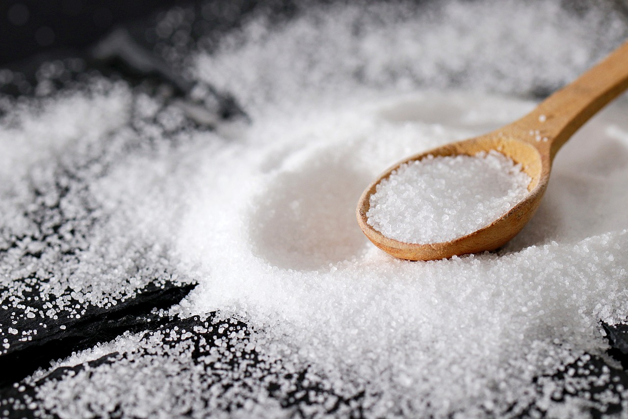 a wooden spoon measuring out a portion of salt. Salt is also surrounding the spoon.